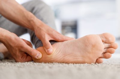 Man hands giving foot massage to yourself after a long walk, suffering from pain in heel spur, close up, indoors. Flat feet, leg fatigue, plantar fasciitis,